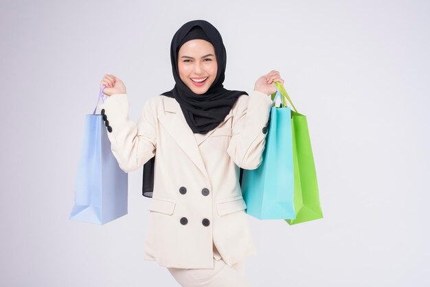Młoda piękna muzułmańska kobieta w garniturze trzymająca kolorowe torby na zakupy na białym tle studio