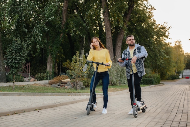Młoda piękna para jeździ na skuterach elektrycznych w parku w ciepły jesienny dzień