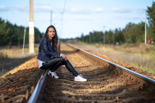Młoda piękna samotna kobieta siedzi na torach kolejowych, czekając na lokomotywę pociągu w pogodny letni dzień
