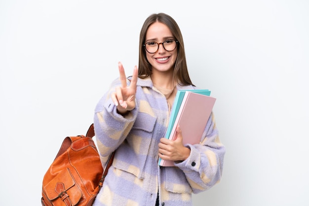 Młoda piękna studentka kobieta odizolowywająca na białym tle uśmiecha się i pokazuje znak zwycięstwa