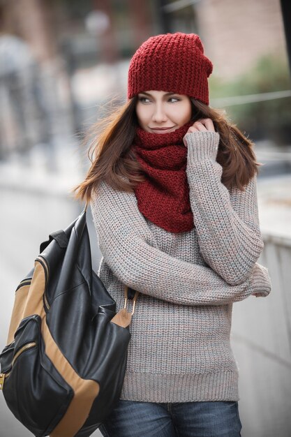 Młoda piękna studentka w dzianym sweterku, czerwonym szaliku i czapce oraz plecaku