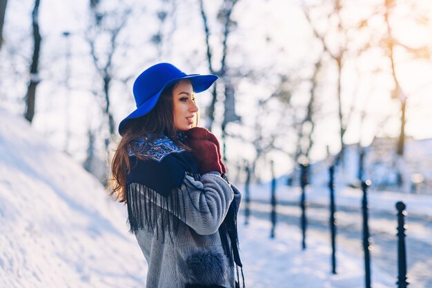 Młoda piękna stylowa kobieta z idealnym uśmiechem w niebieskim kapeluszu i szaliku idąc ulicą