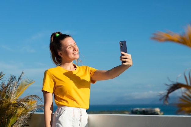 Młoda piękna szczęśliwa blogerka robi sobie selfie przednim aparatem w mediach społecznościowych smartfona telefon komórkowy uśmiecha się machając ręką podczas rozmowy wideo