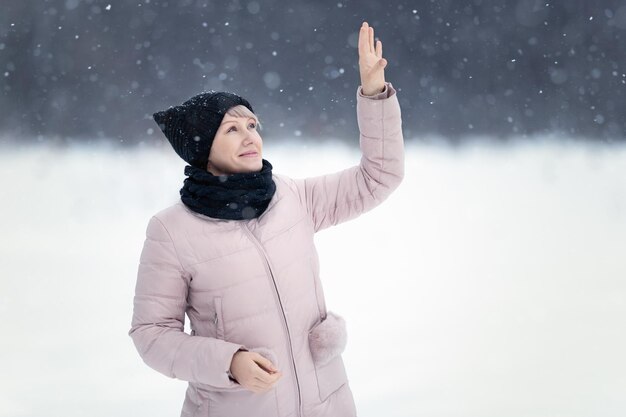 Młoda piękna, szczęśliwa dziewczyna bawiąca się śniegiem łapie płatki śniegu, bawiąc się na świeżym powietrzu w zimowy dzień