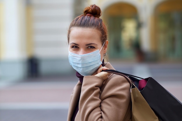 Młoda Piękna Szczęśliwa Kobieta Robi Zakupy W Centrum Handlowym, Ubrana W Ochronną Maskę Medyczną Na Twarzy