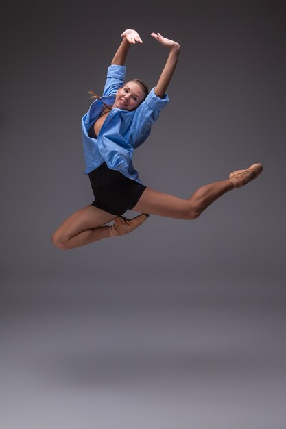 Zdjęcie młoda piękna tancerka w nowoczesnym stylu w niebieskiej koszuli, skacząca na szarym tle studyjnym