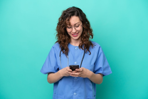 Młoda pielęgniarka kaukaska kobieta na białym tle na niebieskim tle wysyła wiadomość za pomocą telefonu komórkowego