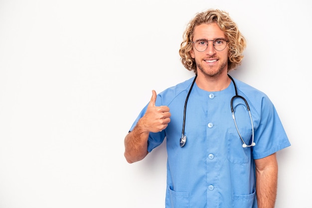 Młoda pielęgniarka kaukaski mężczyzna na białym tle uśmiechający się i podnoszący kciuk w górę