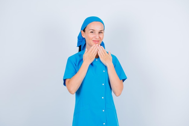 Młoda pielęgniarka pozuje do kamery, trzymając się za ręce przed brodą na białym tle