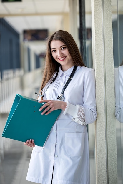 Zdjęcie młoda pielęgniarka stoi ze stetoskopem i trzyma w rękach czasopisma medyczne i książki
