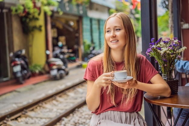 Młoda podróżniczka pije wietnamską kawę z jajkiem siedząc przy torach kolejowych, które przechodzą
