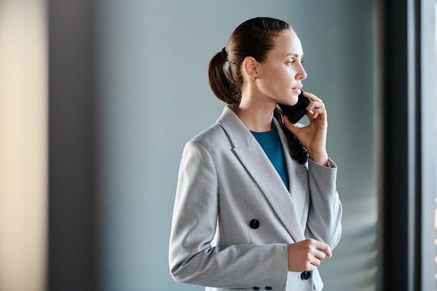 Młoda poważna bizneswoman w stroju formalnym trzymająca smartfon za ucho