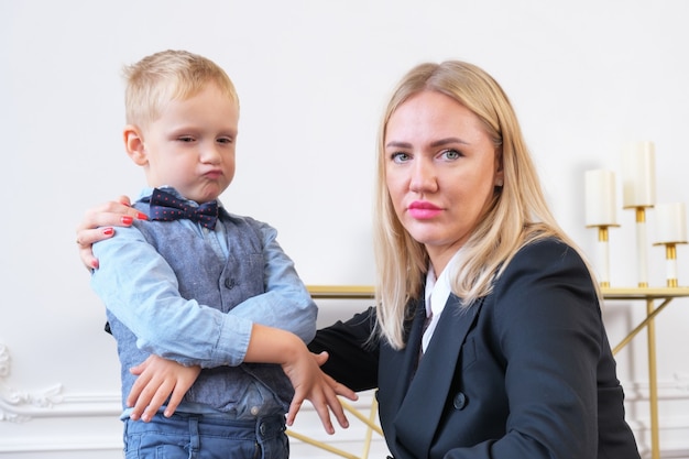 Młoda poważna blondynka w czarnej marynarce i mały chłopiec przedstawiający biznesmena