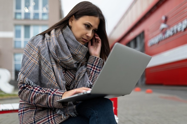 Młoda poważna kobieta interesu skupiona na pracy na laptopach na tle miasta w