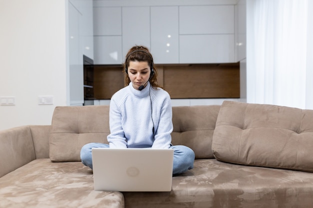 Młoda pracownica call center udziela konsultacji on-line siedząc w domu na kanapie