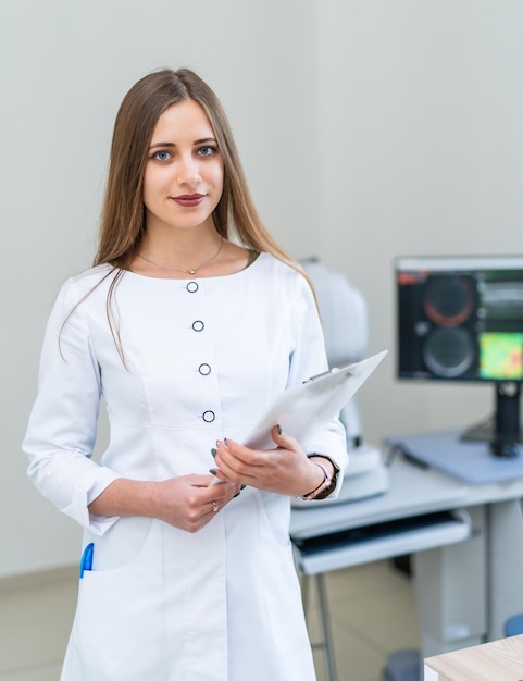 Młoda Profesjonalna Kobieta Lekarz W Białych Zaroślach Pozuje We Wnętrzu Nowoczesnej Kliniki.