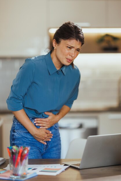 Młoda przedsiębiorczyni cierpi na menstruacyjne skurcze żołądka podczas pracy w domowym biurze.