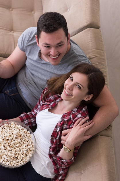 młoda przystojna para ciesząca się wolnym czasem oglądając telewizję z popcornem w swojej luksusowej willi