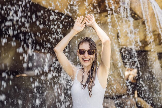 Młoda radosna kobieta pod strumieniem wody w basenie dziennym w spa gorących źródeł