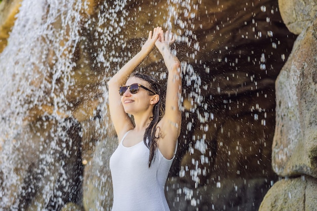 Młoda radosna kobieta pod strumieniem wody w basenie dziennym w spa gorących źródeł