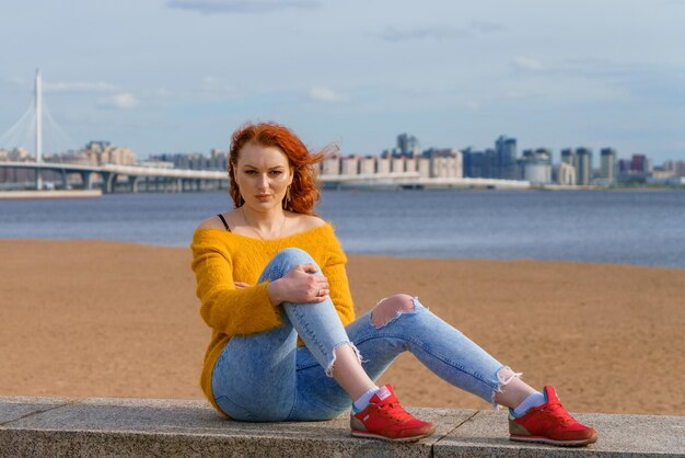 Młoda redhaired dziewczyna w żółtym pulowerze i cajgach Ładna kobieta siedzi