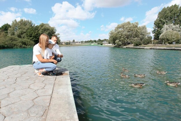 Młoda rodzina karmi dzikie kaczki siedząc na pomoście nad jeziorem