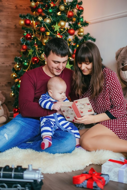 Młoda Rodzina świętująca Boże Narodzenie W Pobliżu Choinki Prezent Dla Małego Dziecka Wszyscy Są Radośni!