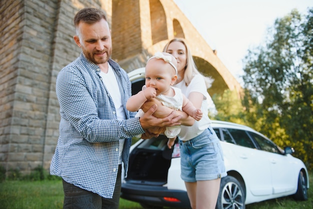 Młoda rodzina trzy osoby w białych ubraniach mają piknik. Piękni rodzice i córka podróżują samochodem podczas letnich wakacji. Scena w parku