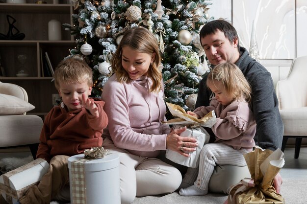 Młoda Rodzina Z Dwójką Małych Dzieci Rozpakowuje Prezenty Przy Choince W święta. Radość I Szczęście W Boże Narodzenie I Nowy Rok.