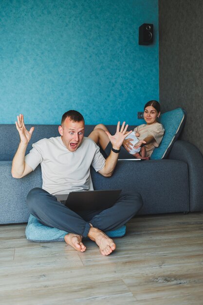 Młoda rodzina z dzieckiem pracuje na laptopie w domu siedząc na kanapie Rodzice z dzieckiem siedzącymi na kanapie w domu z laptopem i rozmawiającymi online