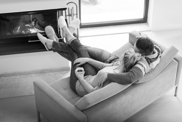 Młoda romantyczna para siedzi na kanapie przed kominkiem w domu, patrząc na siebie, rozmawiając i pijąc kawę jesienny dzień