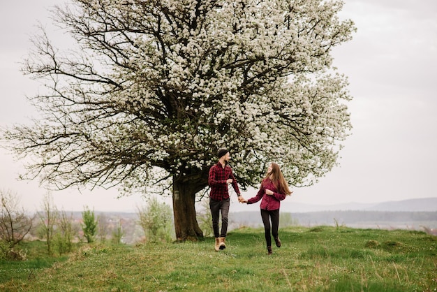 Młoda romantyczna para spacerująca po łące i kwitnącym drzewie i baw się dobrze