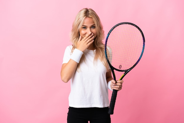 Młoda Rosjanka gra w tenisa na białym tle na fioletowym tle szczęśliwa i uśmiechnięta obejmująca usta rękami