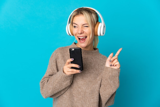 Młoda Rosjanka na niebieskim tle słuchania muzyki z telefonu komórkowego i śpiewu