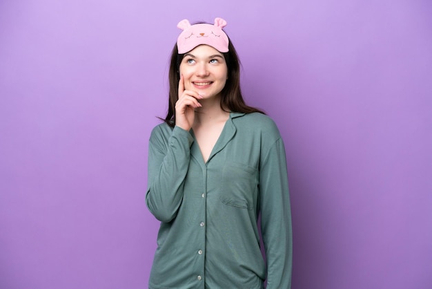 Młoda Rosjanka w piżamie na fioletowym tle myśli o pomyśle, patrząc w górę