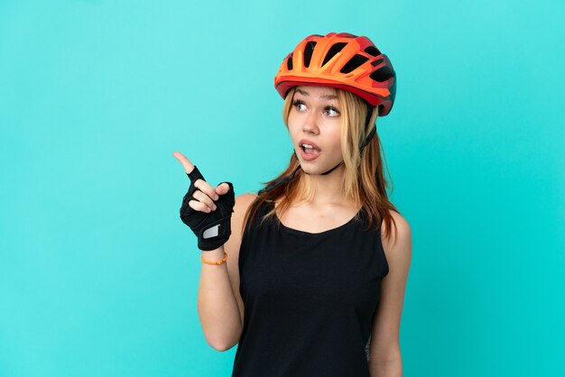 Młoda rowerzystka na odosobnionym niebieskim tle, zamierzająca zrealizować rozwiązanie, podnosząc palec w górę