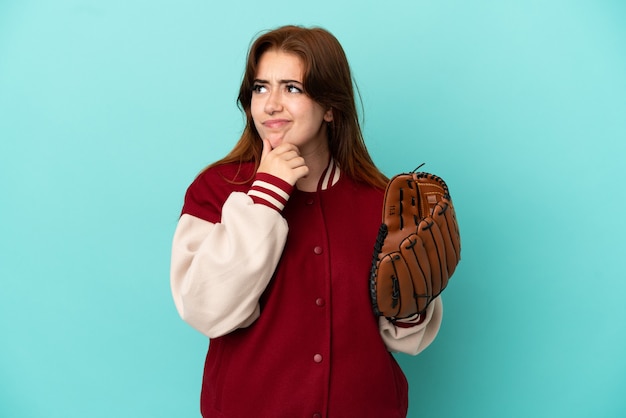 Młoda ruda kobieta gra w baseball na białym tle na niebieskim tle, mając wątpliwości i myśli