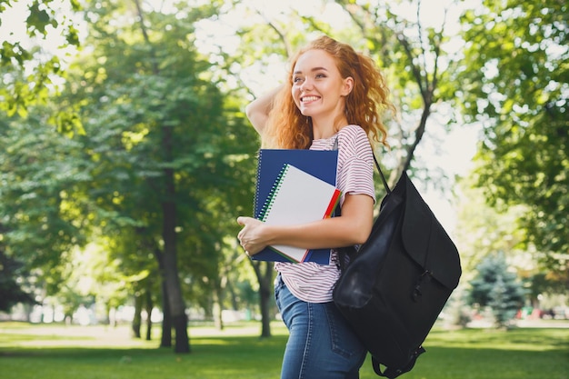 Młoda ruda na zewnątrz. Studentka spaceru w parku z zeszytem i plecakiem. Koncepcja edukacji