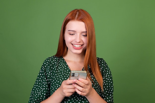 Młoda Rudowłosa Kobieta Na Zielonej ścianie Z Telefonem Komórkowym Wysyłająca Sms-y Na Czacie Z Uśmiechem Na Twarzy, Szczęśliwy Pozytyw