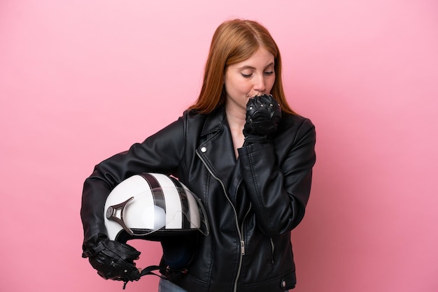 Młoda rudowłosa kobieta w kasku motocyklowym na białym tle na różowym tle ma wątpliwości