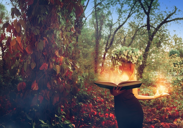 Młoda rudowłosa oszałamiająca wiedźma czyta magiczną książkę w lesie na zewnątrz