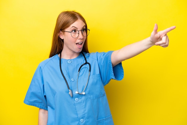 Młoda rudowłosa pielęgniarka kobieta odizolowana na żółtym tle, wskazując daleko