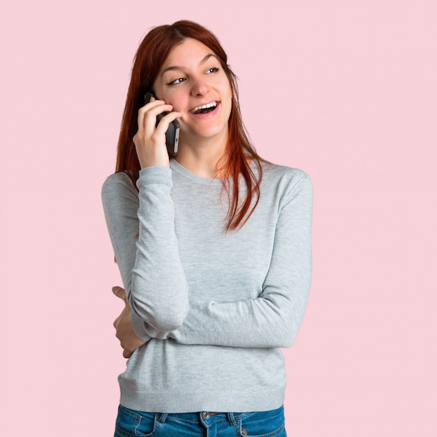 Młoda rudzielec dziewczyna utrzymuje rozmowę z telefonem komórkowym z someone na odosobnionym różowym backgr