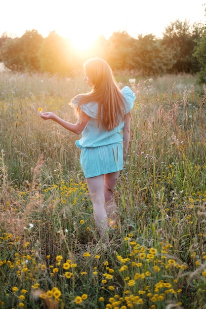 Młoda rudzielec kobieta w błękit sukni odprowadzeniu w zmierzchu polu w lecie.