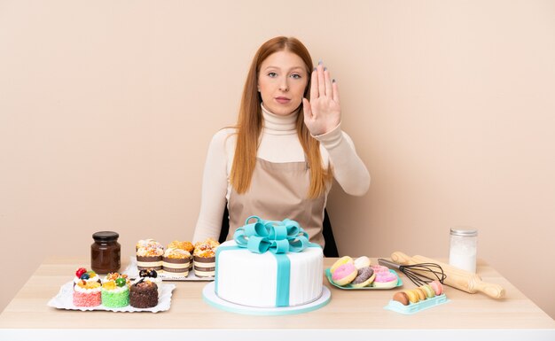 Młoda rudzielec kobieta z dużym tortem robi przerwie gestykulować jej ręką