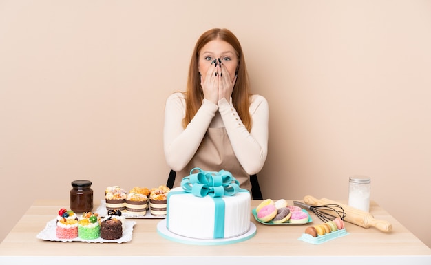 Młoda rudzielec kobieta z dużym tortem z niespodzianka wyrazem twarzy