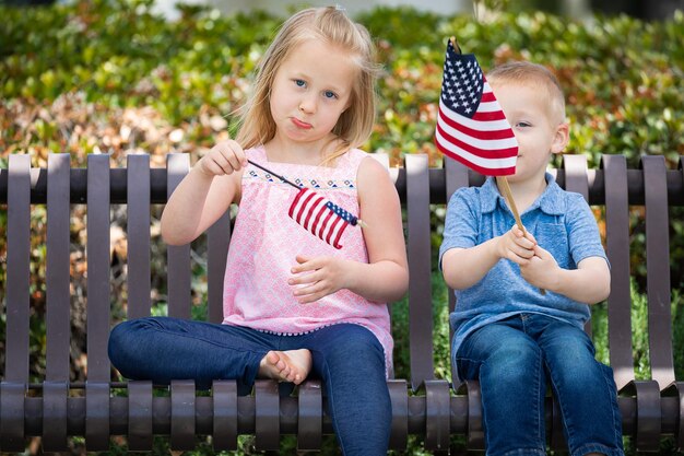 Zdjęcie młoda siostra i brat porównują rozmiar amerykańskiej flagi na ławce w parku