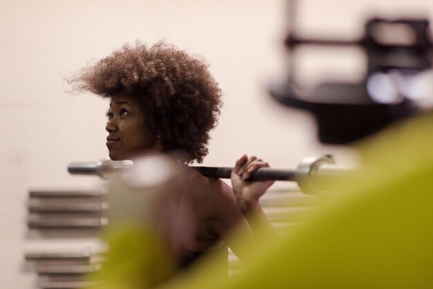 Młoda śliczna african american kobieta sport w sali fitness podnosząca pusty bar