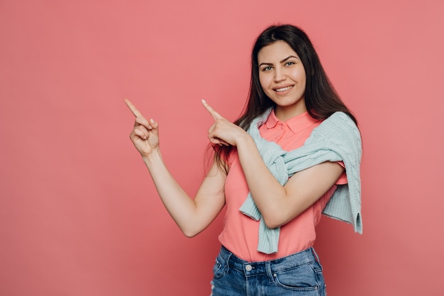 Młoda śliczna brunetka ubrana w różowy t-shirt i turkusowy sweter zawiązany na ramionach