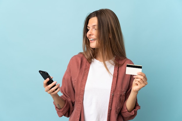 Młoda Słowaczka samodzielnie na niebieskim tle kupowanie za pomocą telefonu komórkowego za pomocą karty kredytowej